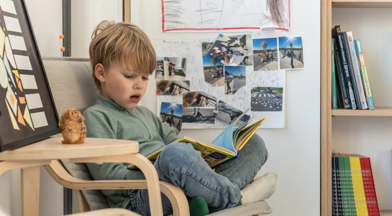 A boy reading in an armchair in front of a wall of photos