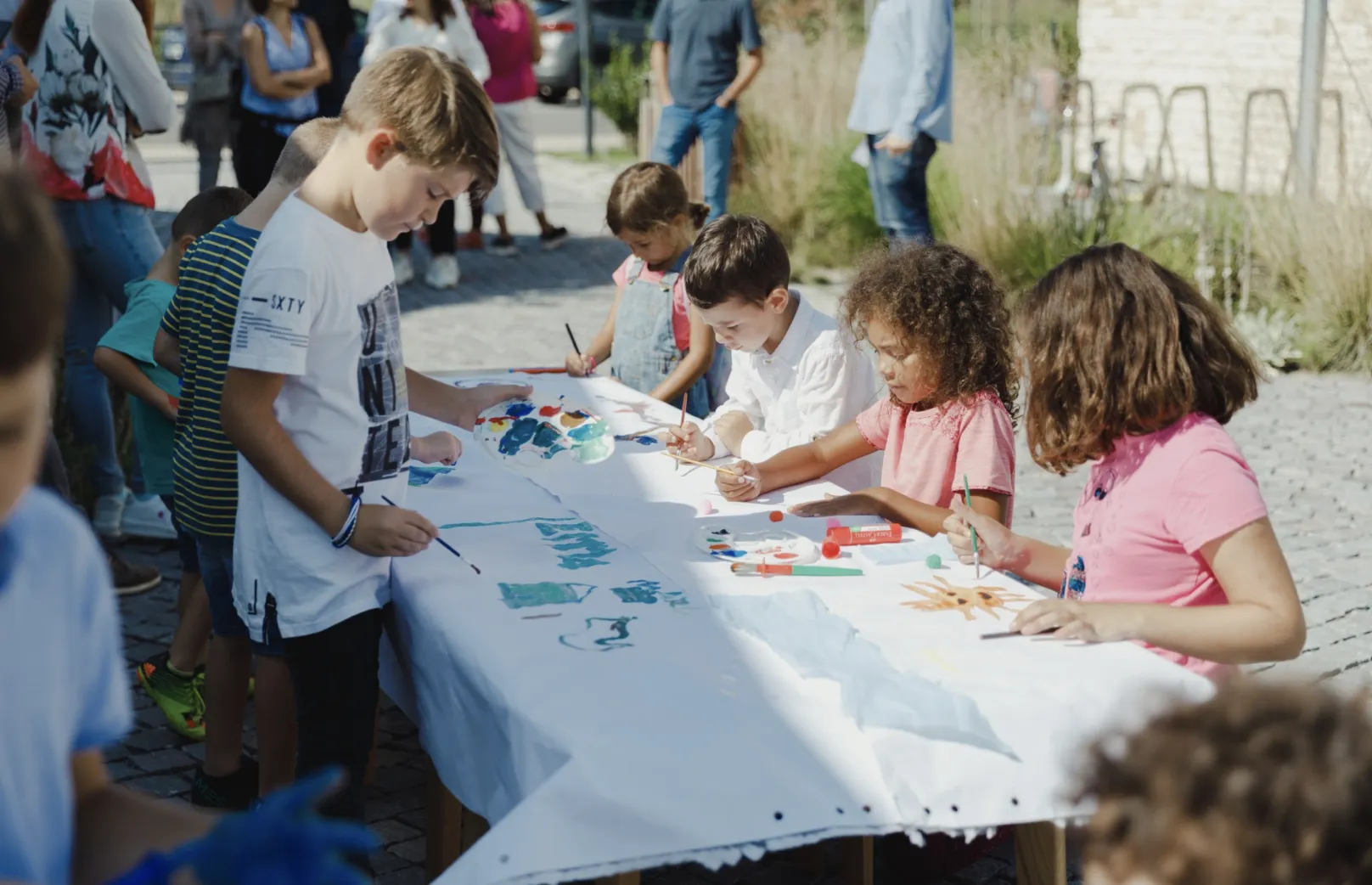 Children painting together at a long table outdoors